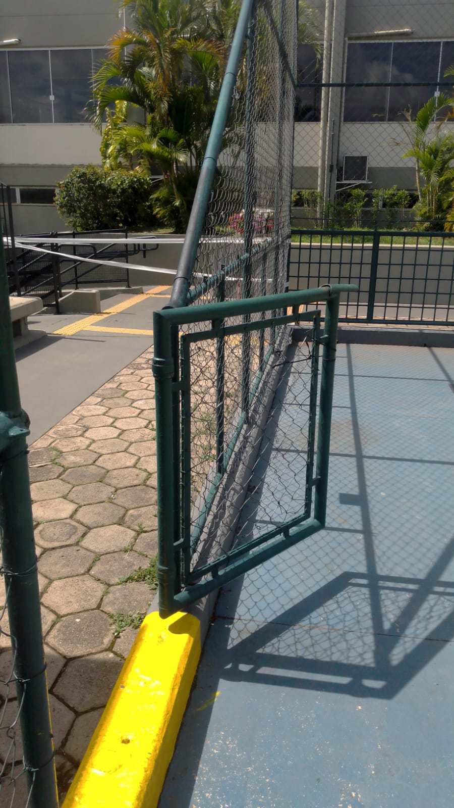 Quadra esportiva com alambrado verde e mureta amarela