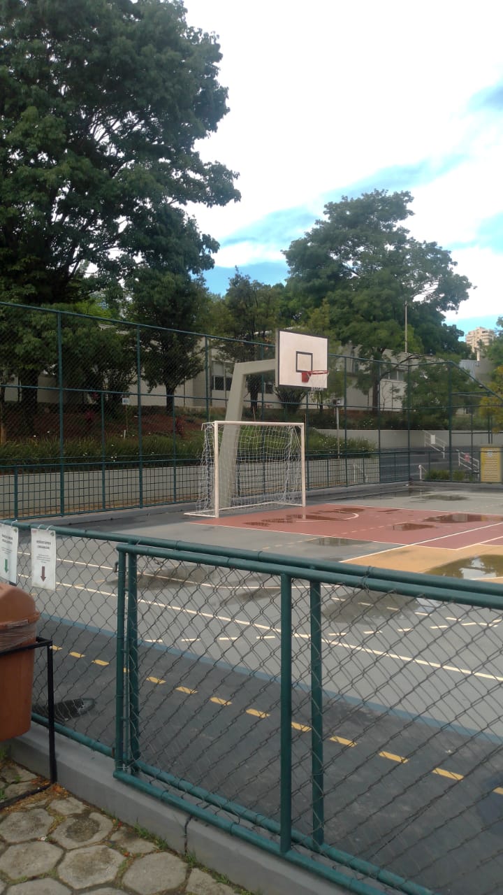 Quadra poliesportiva com alambrado, tabela de basquete e trave de futsal