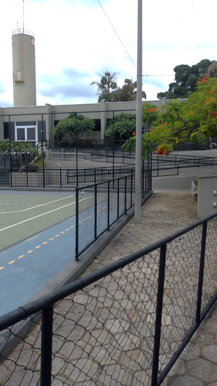 Quadra esportiva cercada com alambrado e caixa d'água ao fundo